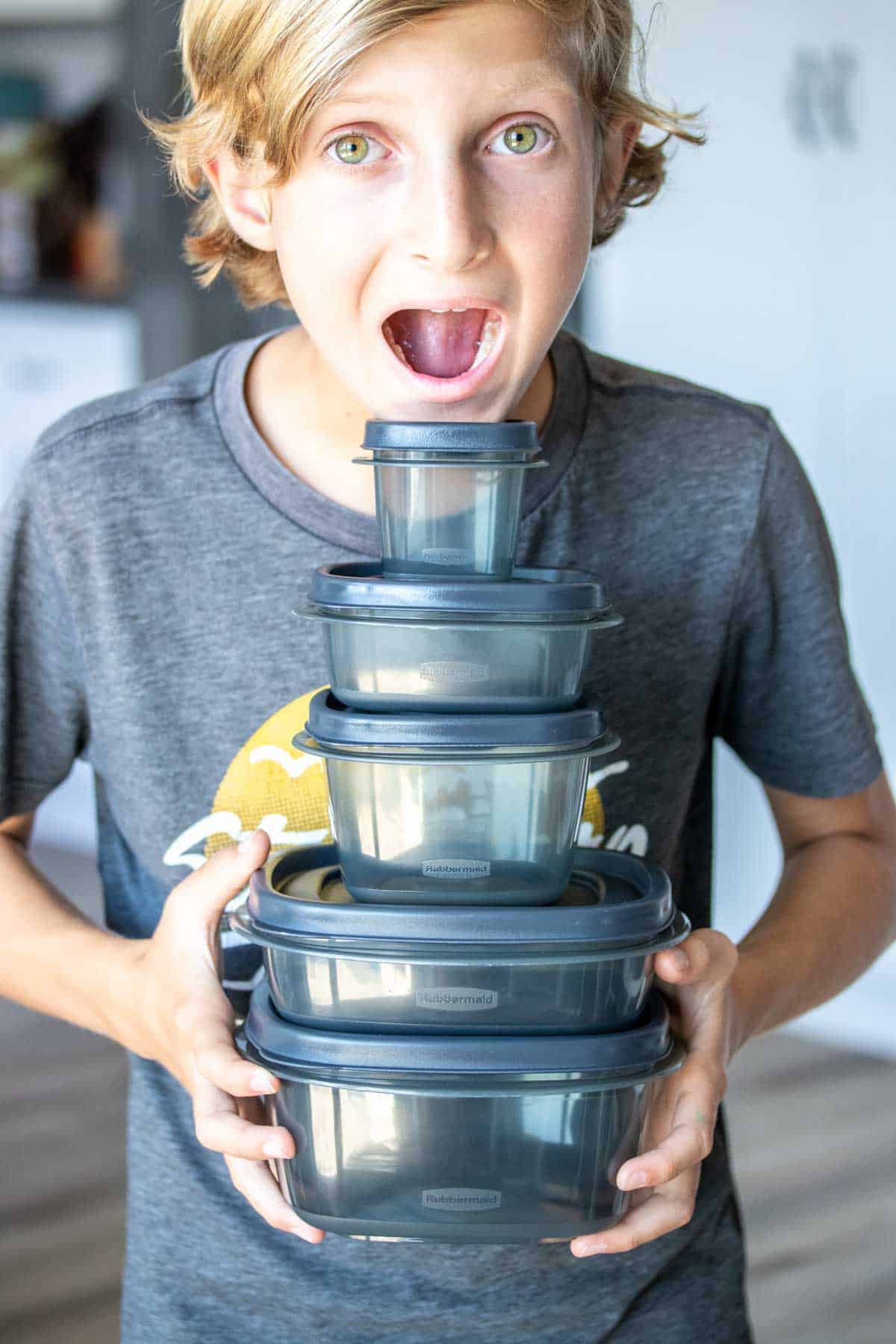A boy with a shocked expression holding a stack of five different sized containers in size order in his hands.