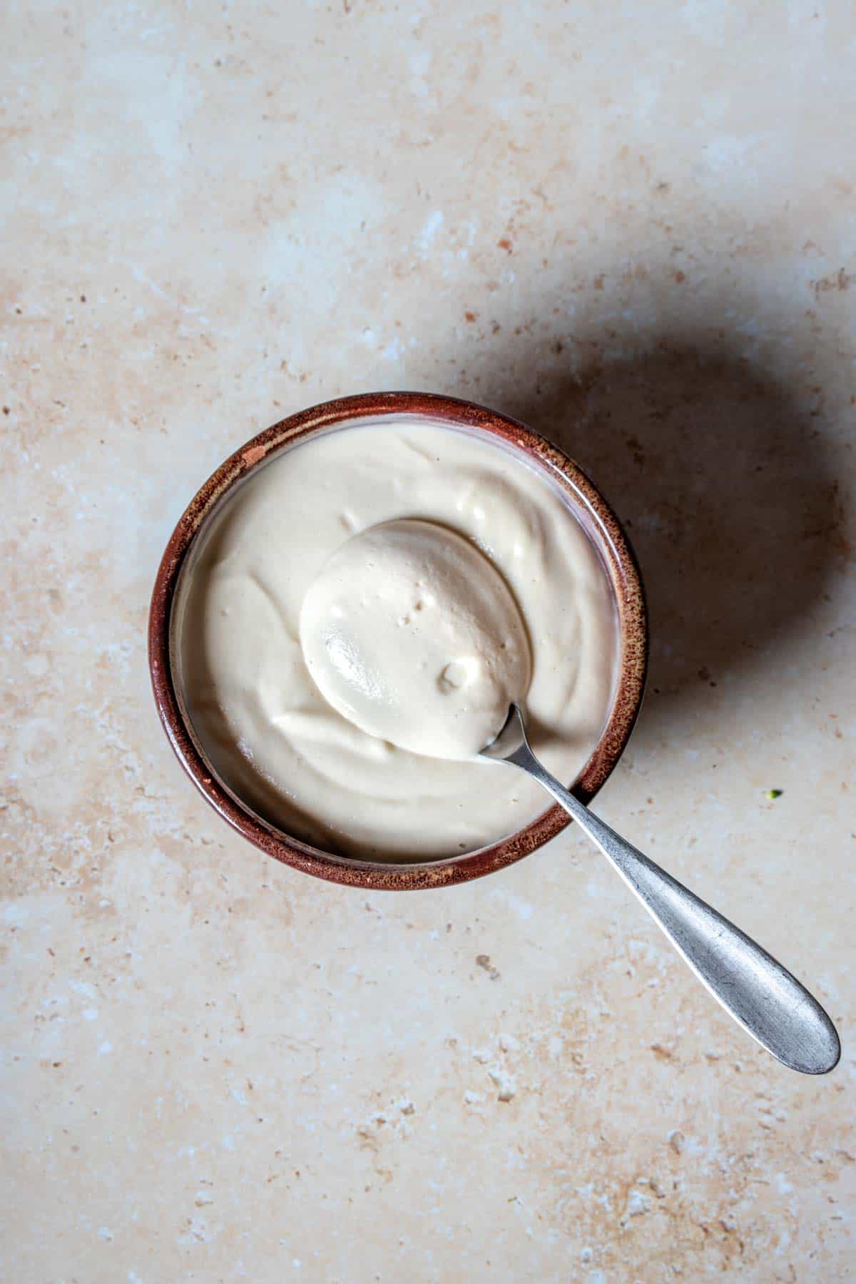 A spoon coming out of a brown bowl filled with a creamy type dressing.