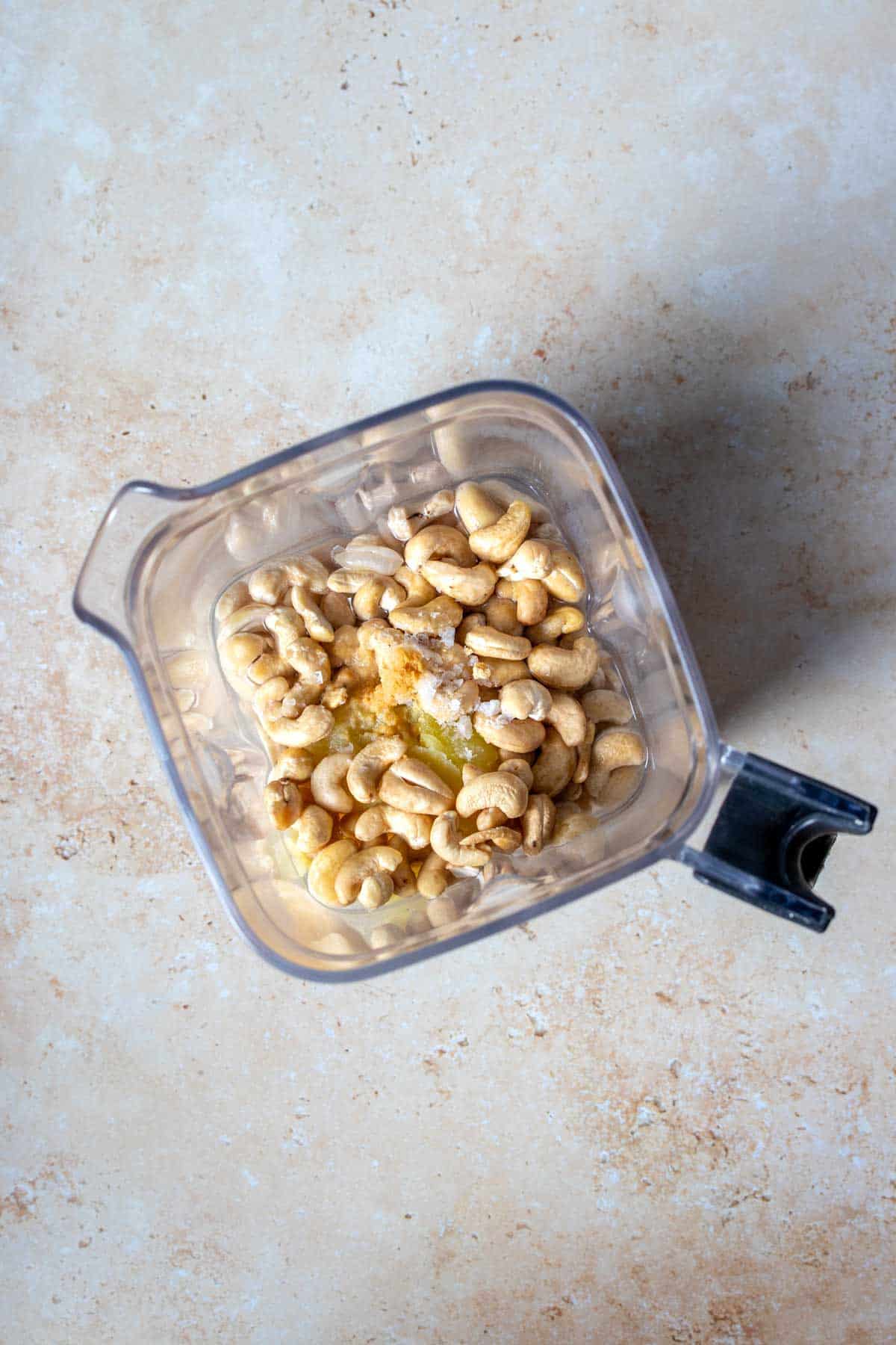 Overhead view of a blender with cashews, potato, spices and white beans and milk underneath.