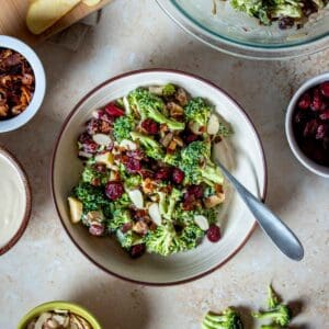 A creamy broccoli salad topped with cranberries and slivered almonds in a tan bowl with a fork.