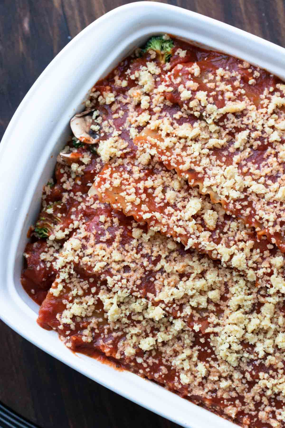 Top view of an uncooked lasagna covered in red sauce and parmesan in a white baking dish.