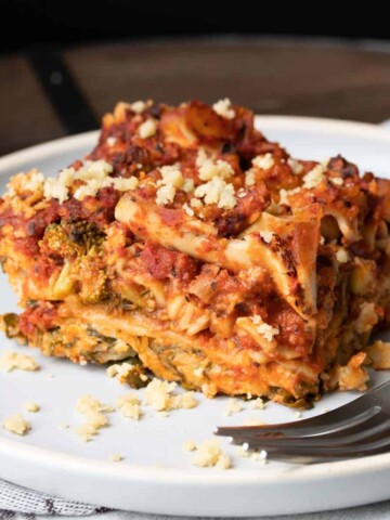 Front view of a piece of lasagna on a white plate with a fork on the plate.