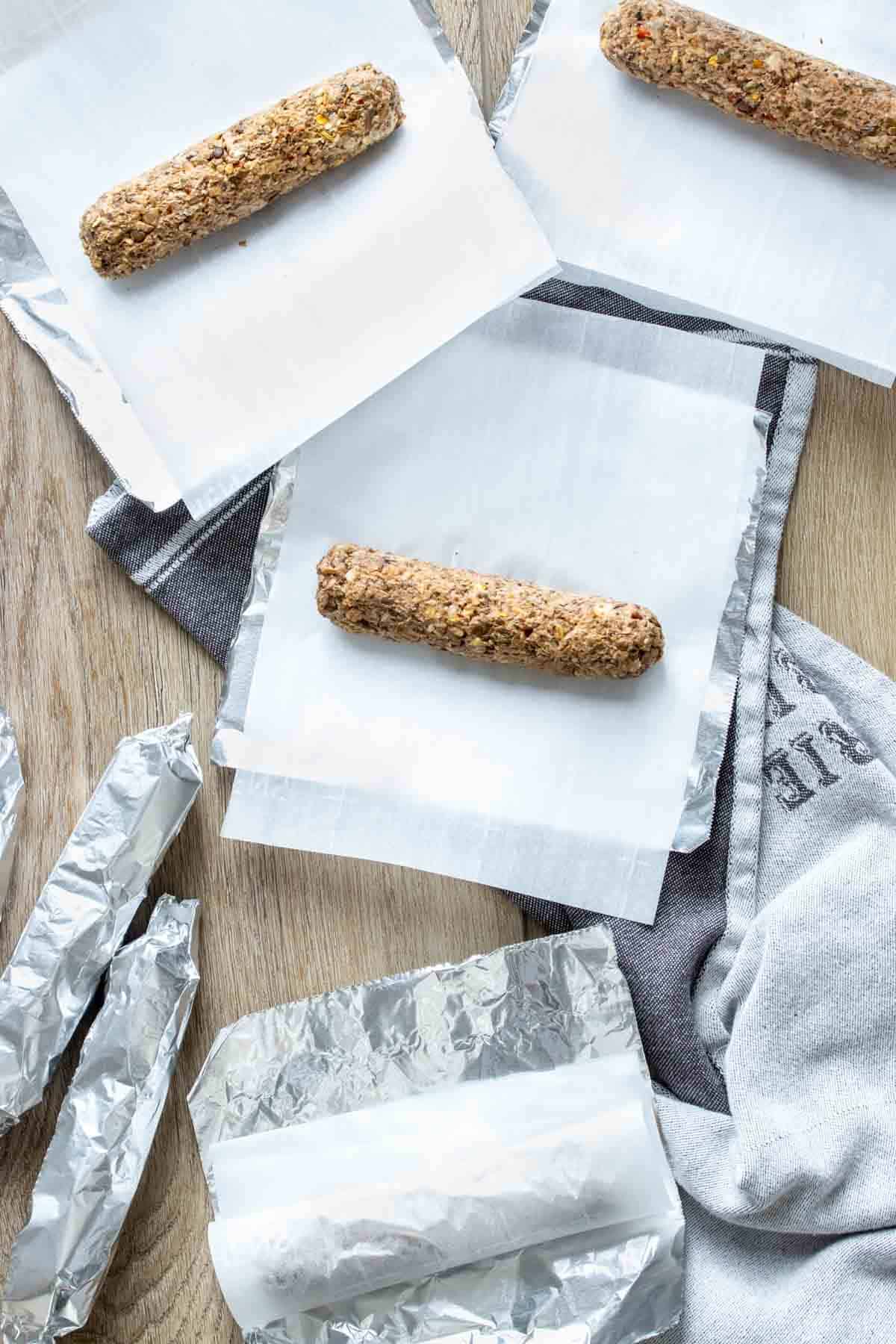 Top view of three uncooked bean based sausages on parchment sitting on foil with three others wrapped already.