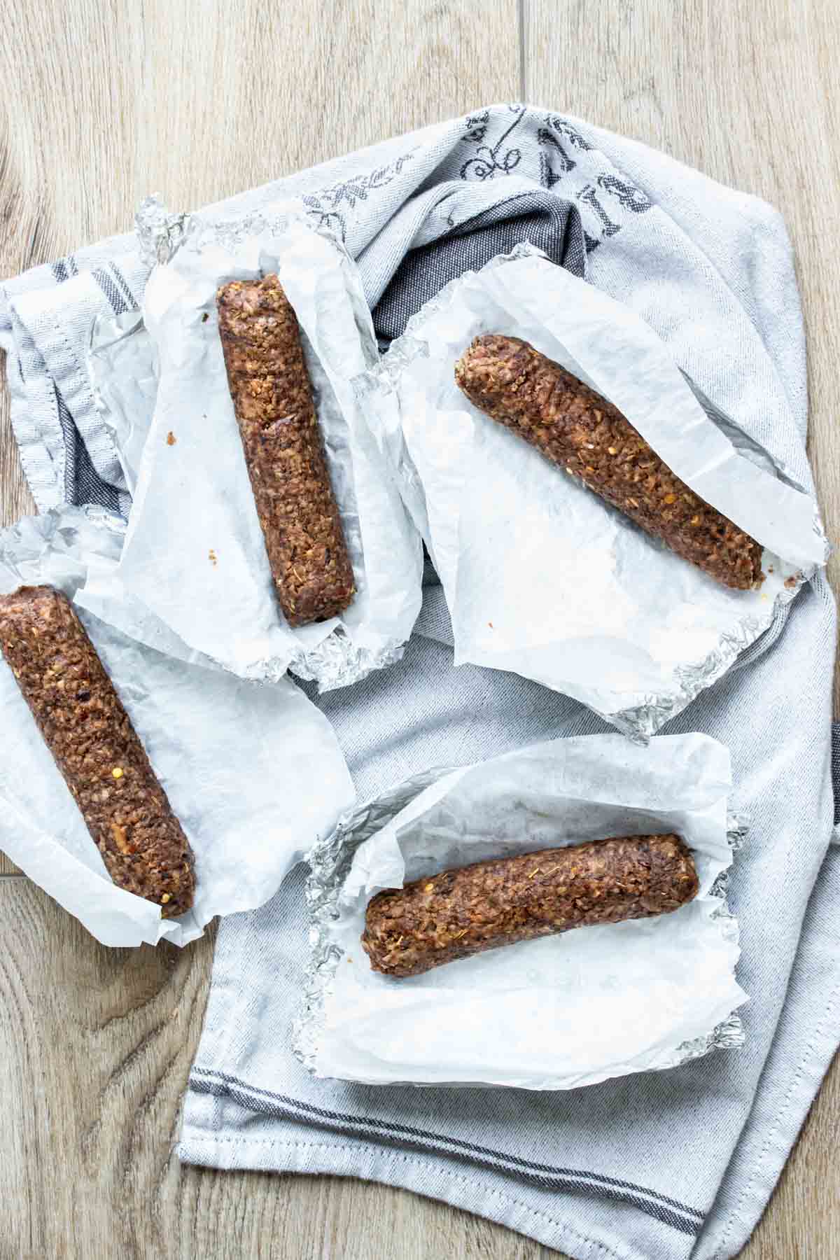 Top view of four sausages in parchment and foil sitting on a grey towel on a wooden surface.