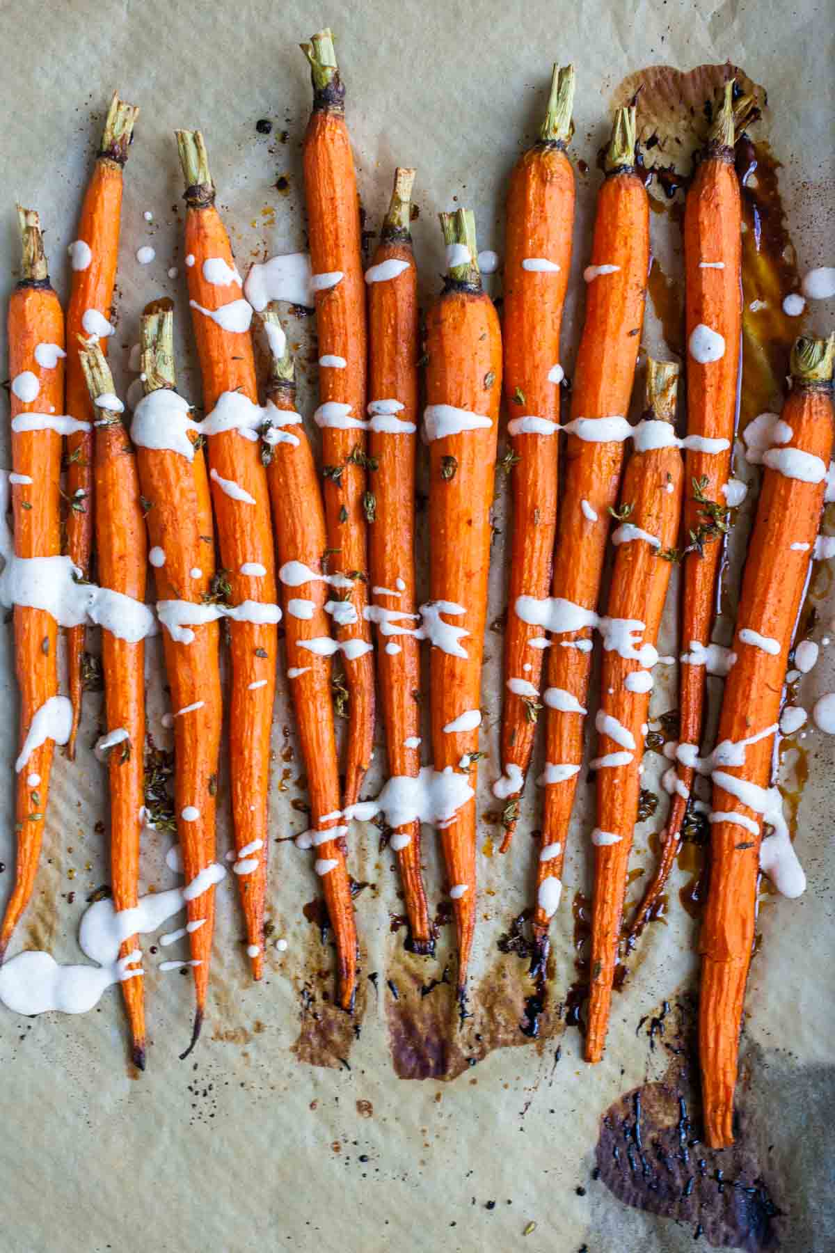 A piece of parchment paper with a line of roasted carrots with a white drizzle and brown baked parts on the parchment.