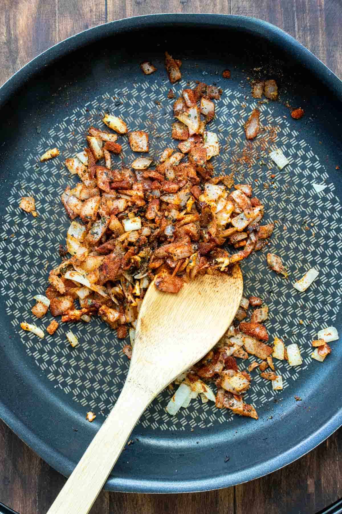 A wooden spoon sautéing onions in a frying pan.