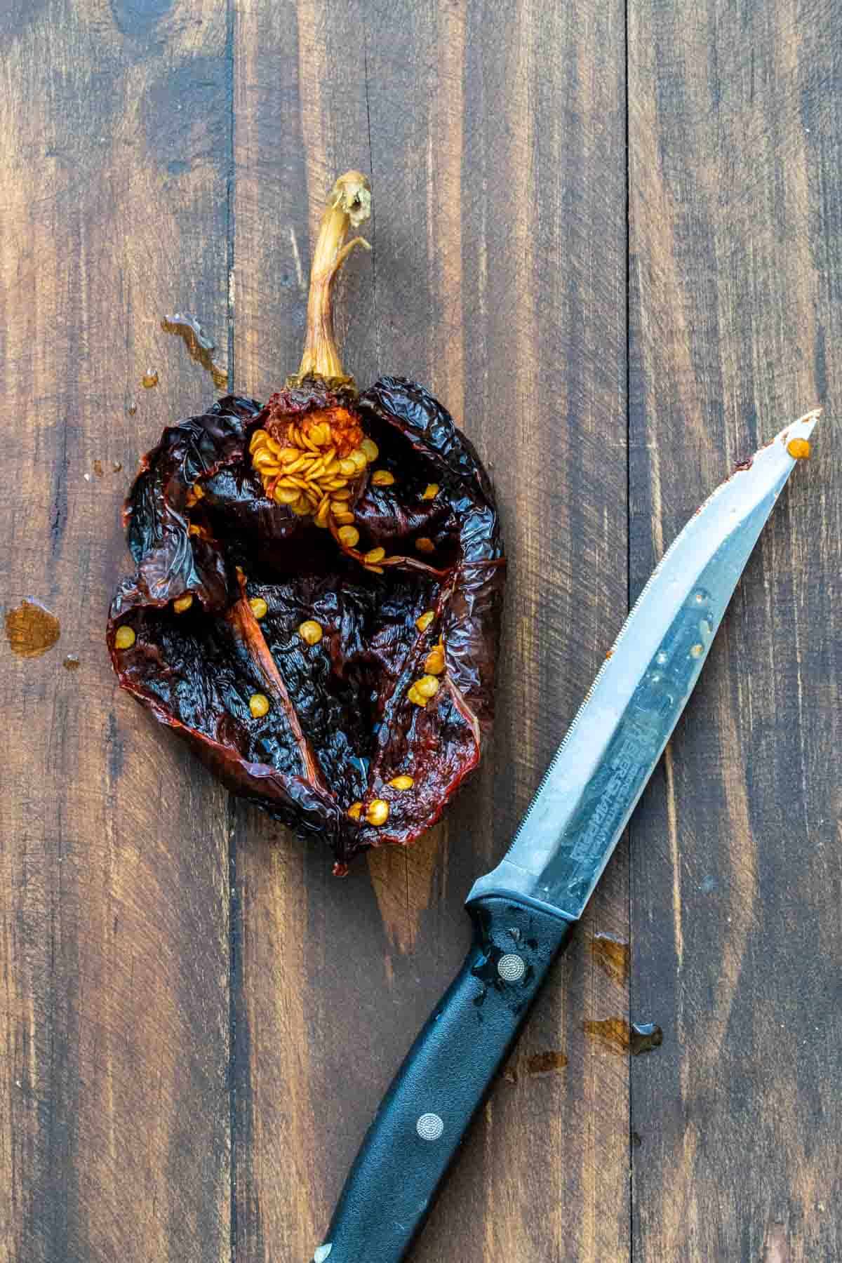 Top view of a soaked dried chili pepper cut open with a knife next to it.