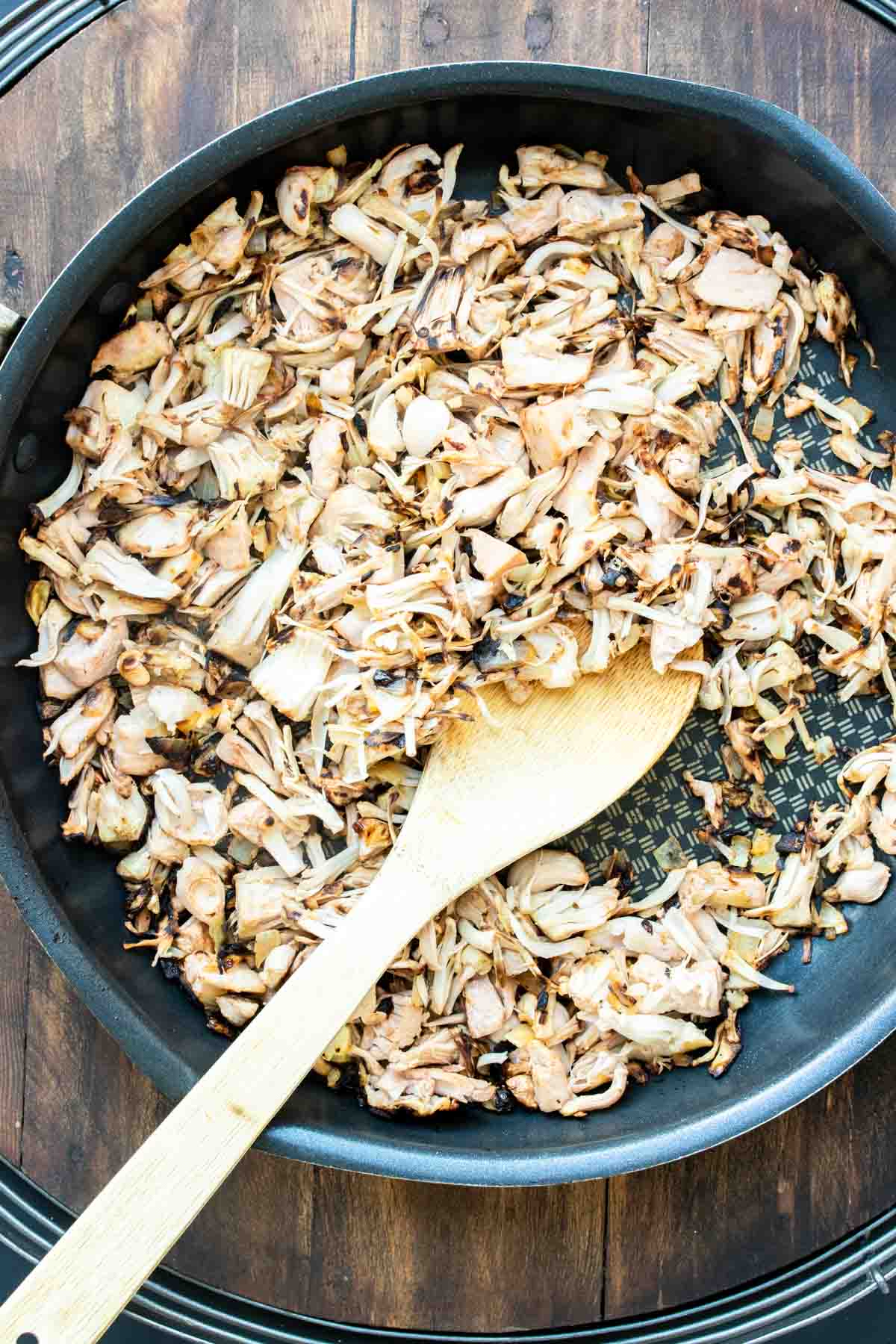 A wooden spoon mixing jackfruit in a frying pan.