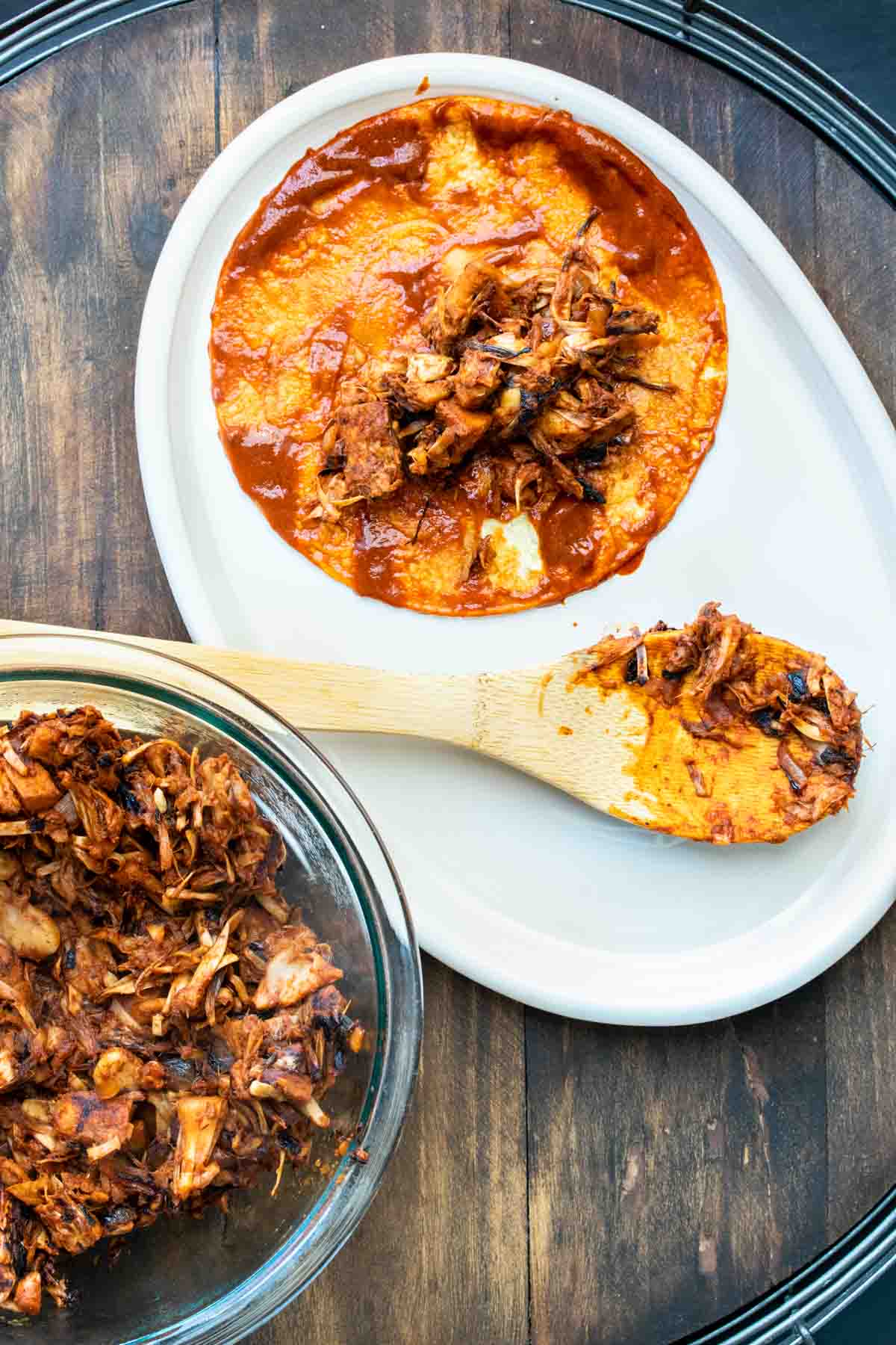 An open faced taco with red sauce and jackfruit in the center sitting on a white platter with a wooden spoon on it.