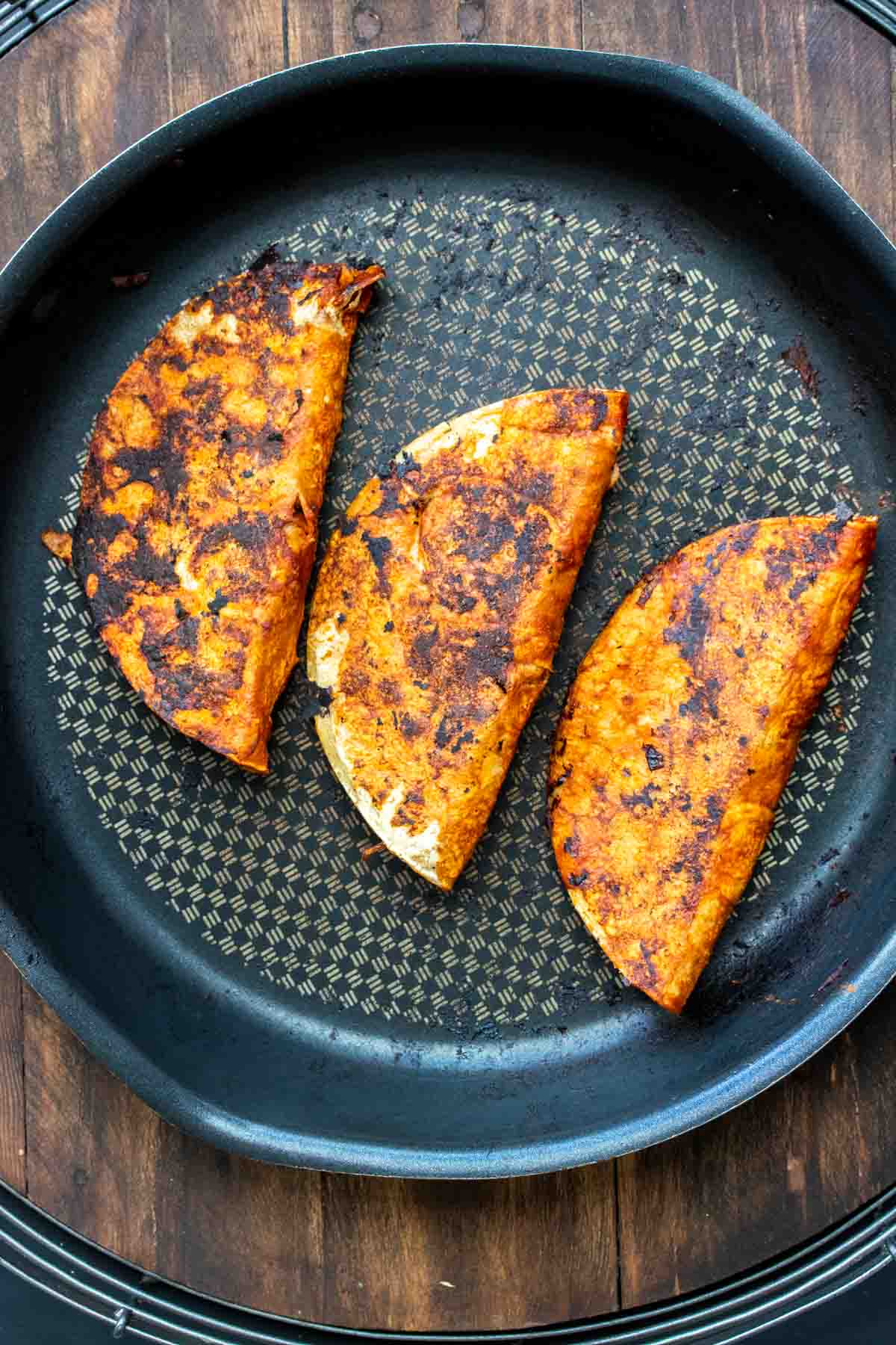 Top view of three tacos grilling on a pan with red sauce on the outside.