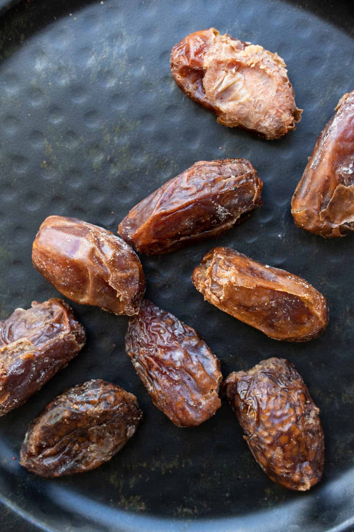 A group of medjool dates laying across a black plate.