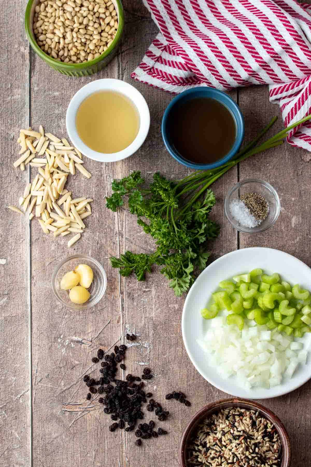 A wooden surface with ingredients needed to make a rice Christmas stuffing and a red striped towel on it.