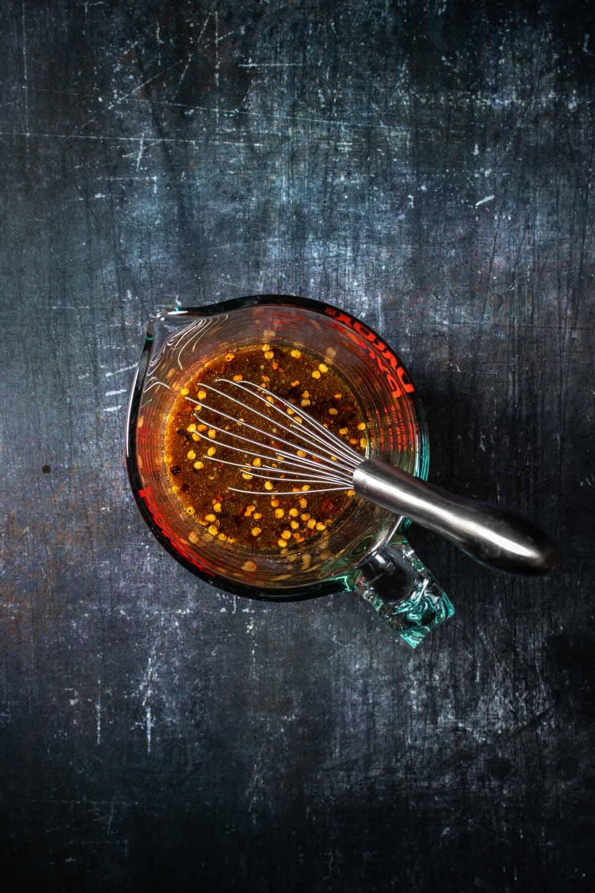 Top view of a glass measuring cup with a brown liquid inside and a whisk in it.