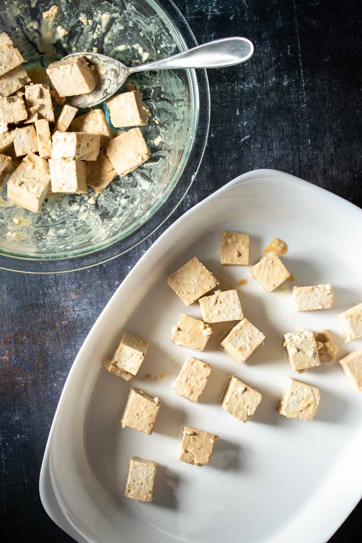 A white baking dish with pieces of tofu covered in a cornstarch coating next to a glass bowl of them.