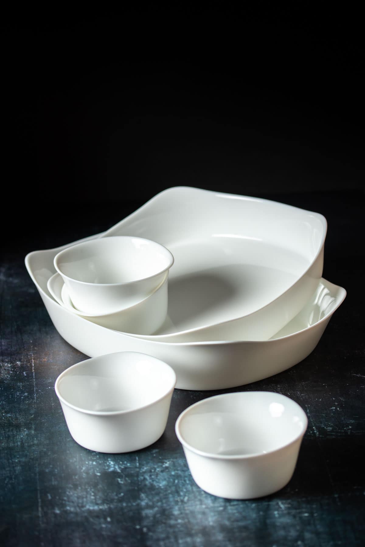 A stacked pile of white baking dishes in different sizes sitting on a dark surface.