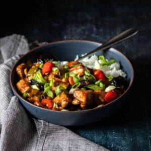 Kung Pao tofu over white rice in a dark blue bowl with a fork in it sitting next to a grey towel.