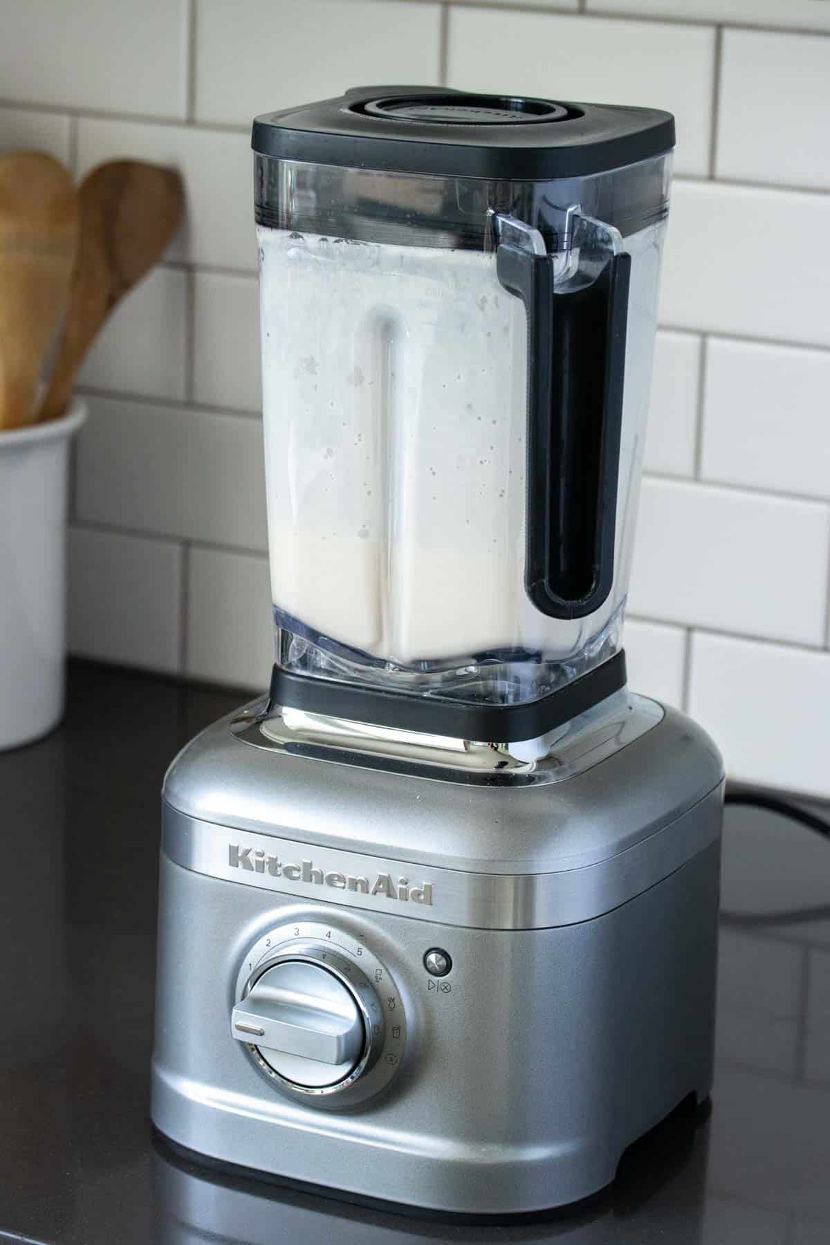 A silver based blender on a grey countertop with white liquid in it.