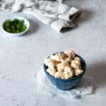 A small blue bowl with cheese curds in it and a small white bowl with chopped parsley in it.