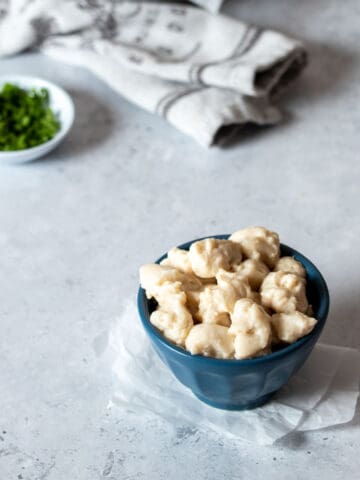 A small blue bowl with cheese curds in it and a small white bowl with chopped parsley in it.