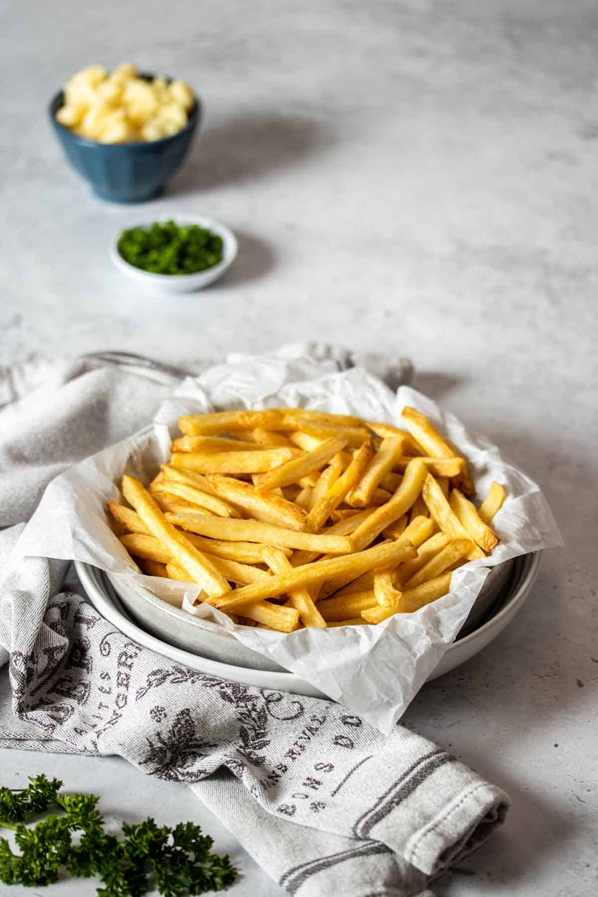Two white bowls stacked on top of each other with parchment paper and french fries in them.