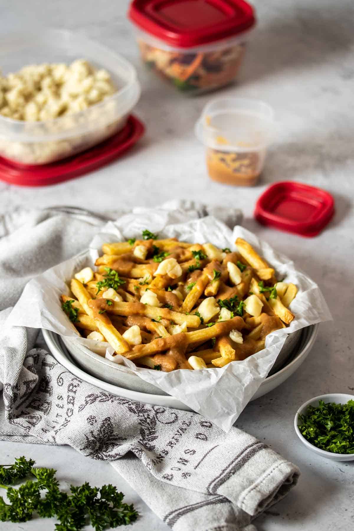 Two stacked bowls with poutine fries in them and three plastic containers with red lids filled with thanksgiving foods in the background.