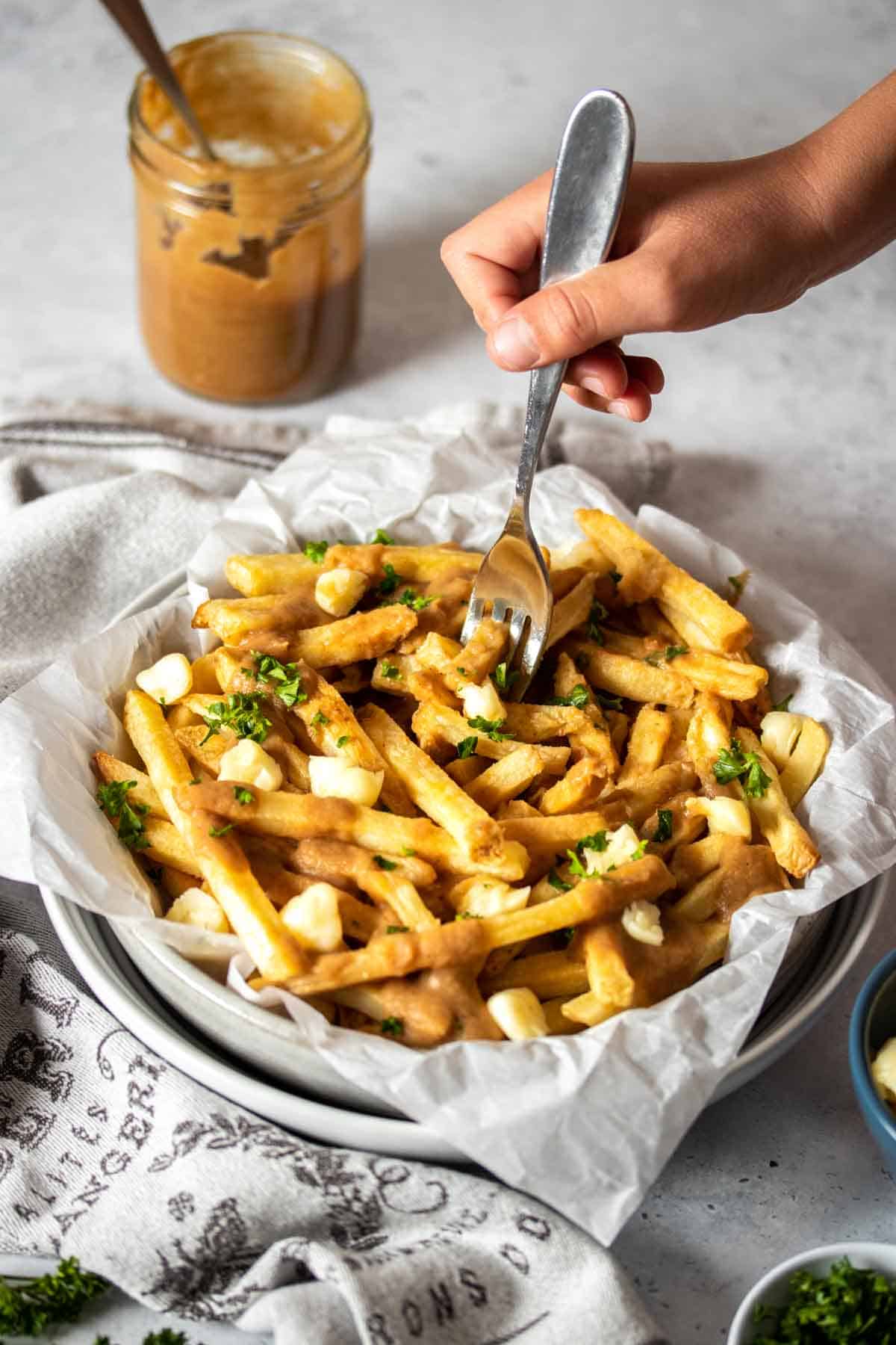 A hand with a fork getting a bite of poutine from two stacked white bowls.