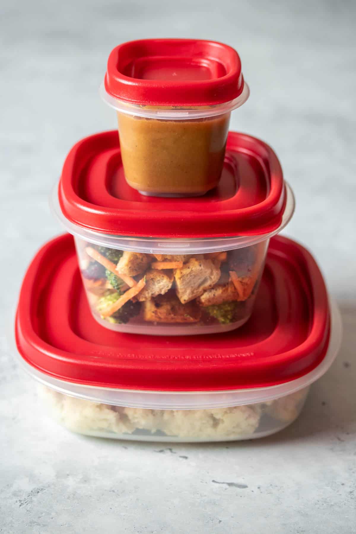 Three plastic containers with red lids stacked going from largest on the bottom to smallest on top.