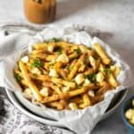 A plateful of poutine on a grey surface with a towel next to the plate.