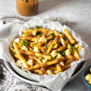 A plateful of poutine on a grey surface with a towel next to the plate.