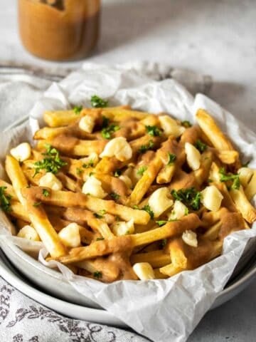 A plateful of poutine on a grey surface with a towel next to the plate.