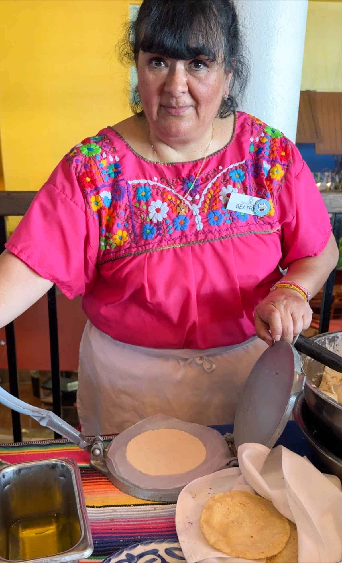 A woman in a hot pink shirt showing how to use a tortilla press to make a homemade corn tortilla.