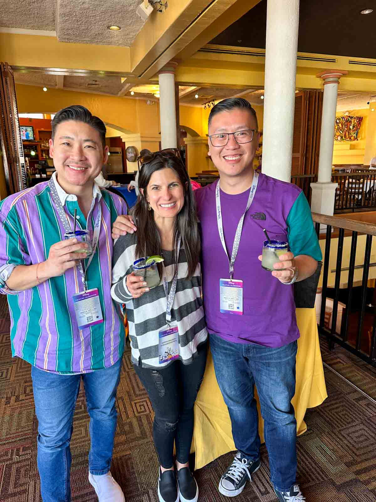 A woman in between two asian men all holding margaritas and smiling at the camera.