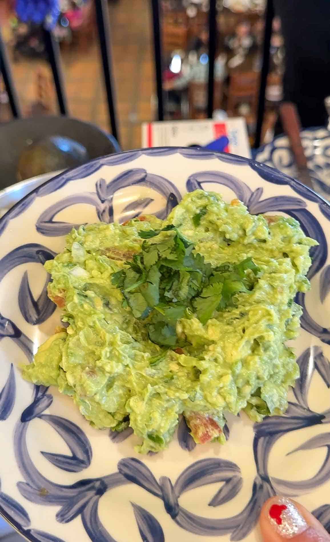 A round portion of guacamole with cilantro on top on a decorative blue and white plate.