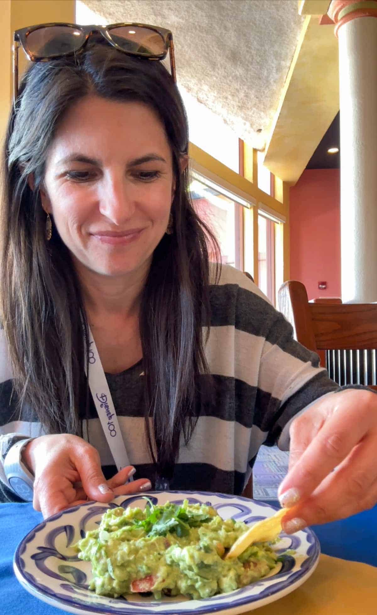 A woman with long brown hair and a striped sweater dipping a chip in a bowl of guacamole.