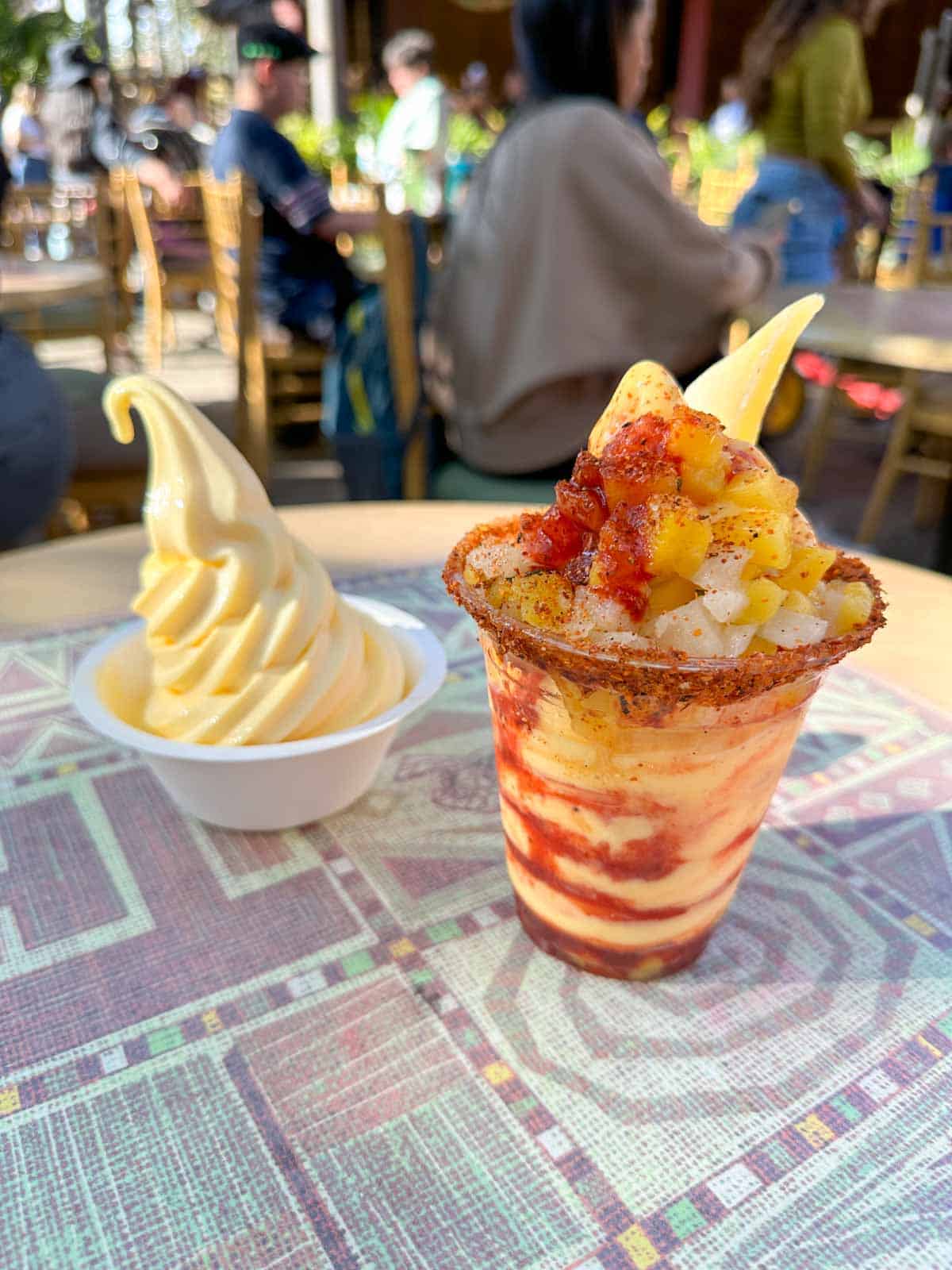 A plain pineapple dole whip and a chile mango flavored dole whip sitting on a table with a mavue and white design.