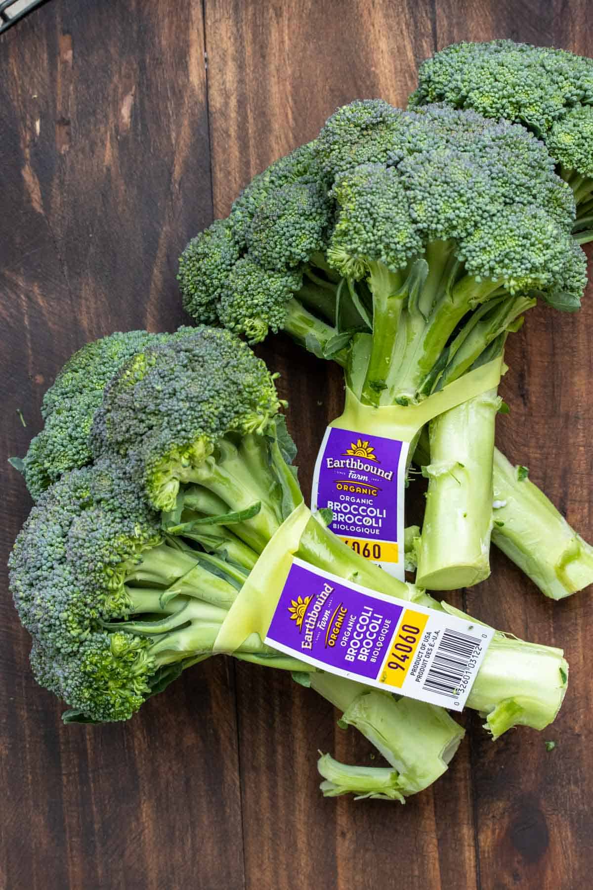 Two sets of heads of broccoli wrapped together laying on a wooden surface.