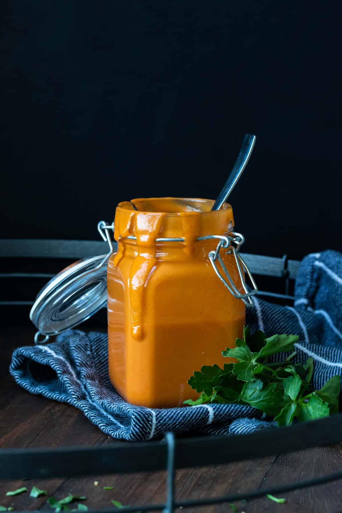 A glass jar with a spoon in it filled with buffalo sauce and dripping out of the jar.