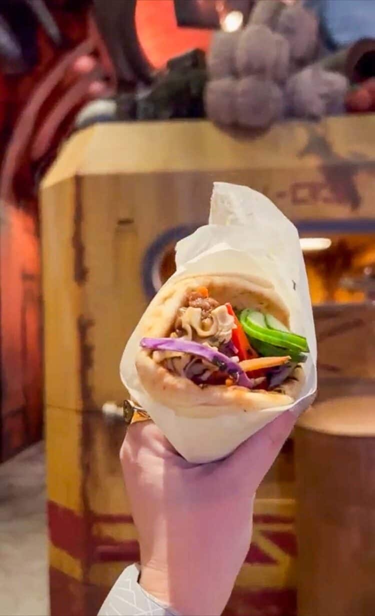 A hand holding a pita bread stuffed with veggies wrapped in parchment paper. 