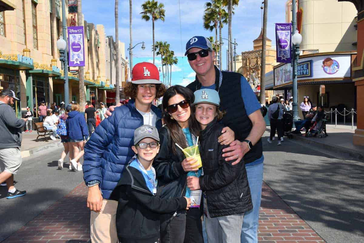 A family of five hugging tight standing in a street at Disney California Adventure and the mom is holding a cup with a frosted drink.