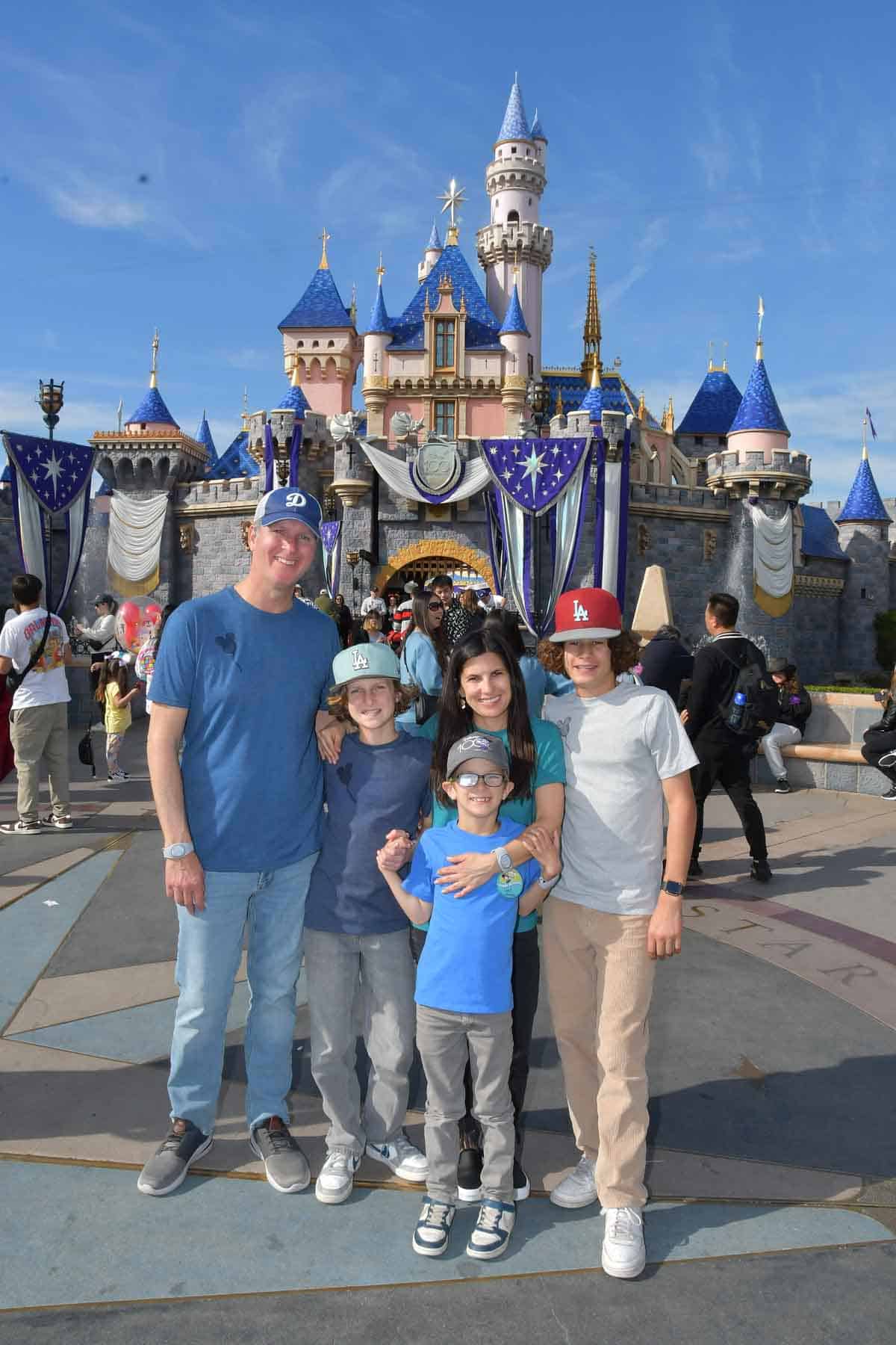 A family of five standing together with arms around each other in front of Cinderella's castle at Disneyland.