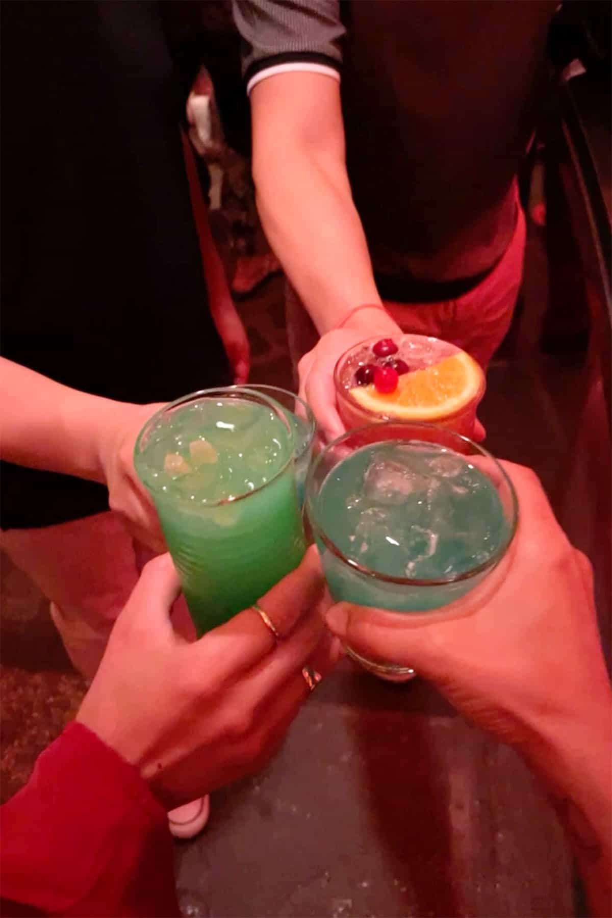 Four hands holding colorful cocktails doing a cheers.