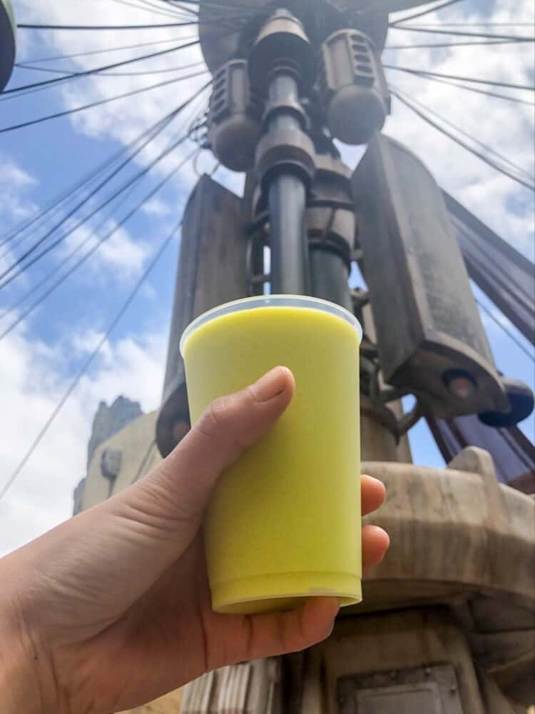 A hand holding a drink that is a creamy light lime green color in front of an object in Star Wars land.