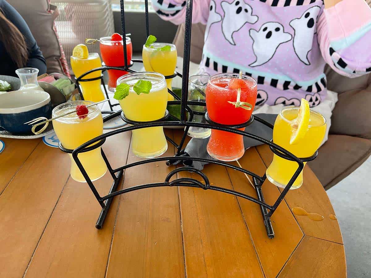 A black wire stand with four different cocktails in it in yellow and one is red.