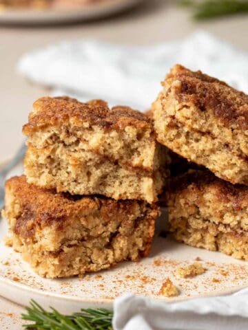 A close up of a tan plate on a tan surface with four pieces of coffee cake on it piled high.