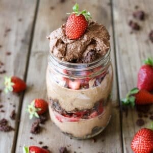 Chocolate mousse layered with strawberries and brownie pieces in a glass mason jar on a wooden surface.