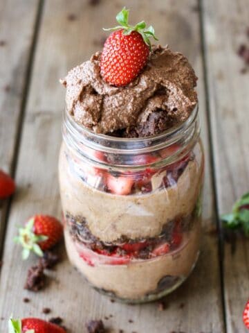 Chocolate mousse layered with strawberries and brownie pieces in a glass mason jar on a wooden surface.