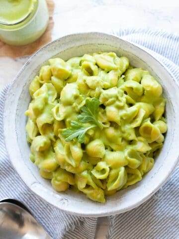 Shell pasta mixed with green cheese sauce in a white bowl with a small leaf on top.