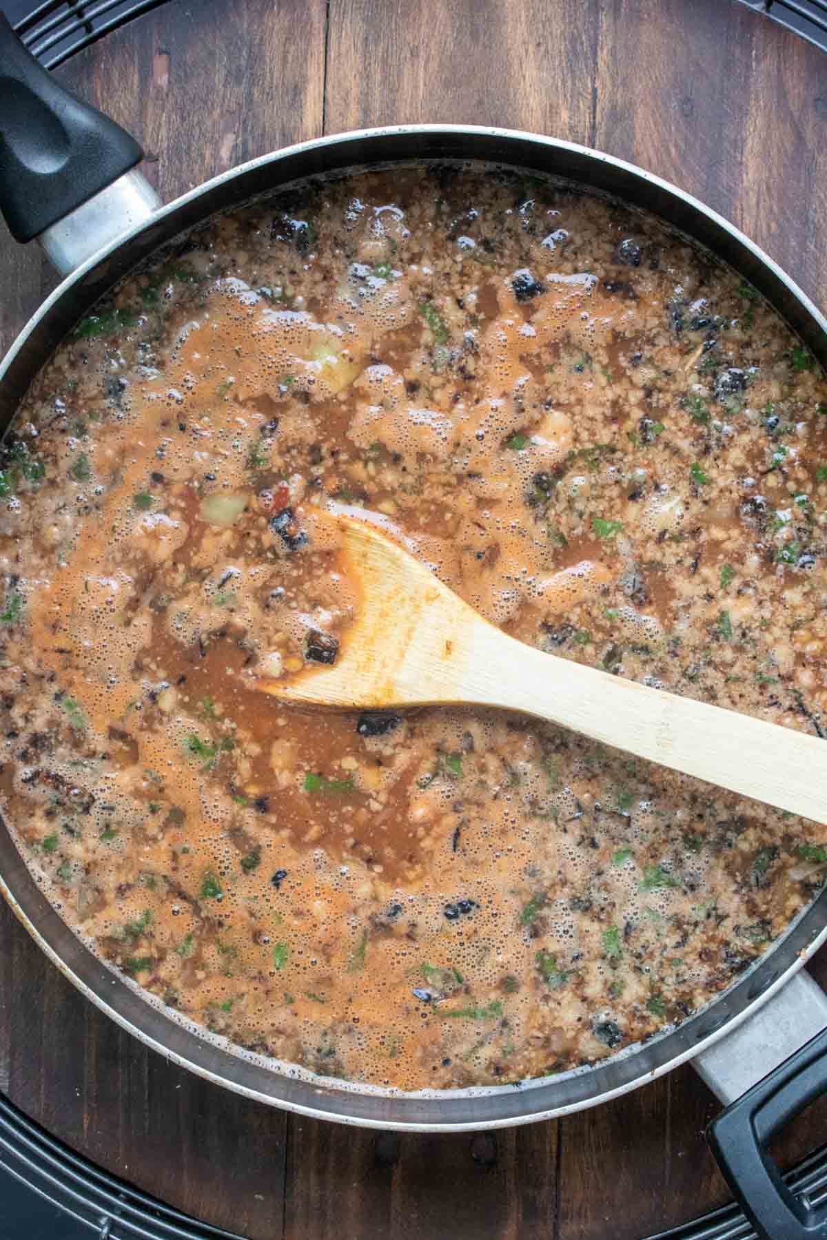 A wooden spoon mixing a brown liquid with lentils in it in a pan.
