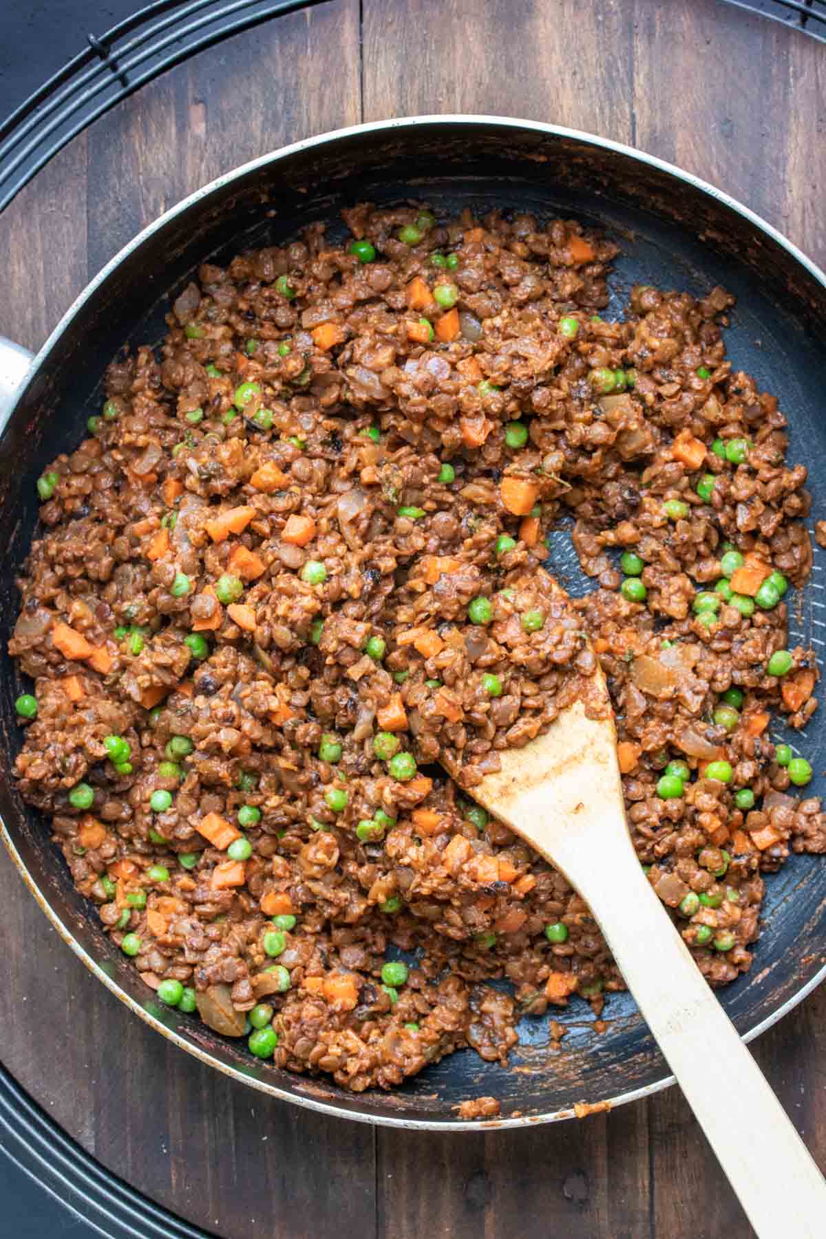 A pan with a bean based crumble with a red brown color mixed with peas and carrots and being mixed.
