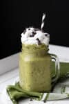 A shamrock shake with chocolate chips in a glass mug topped with whipped cream and a straw in the top.